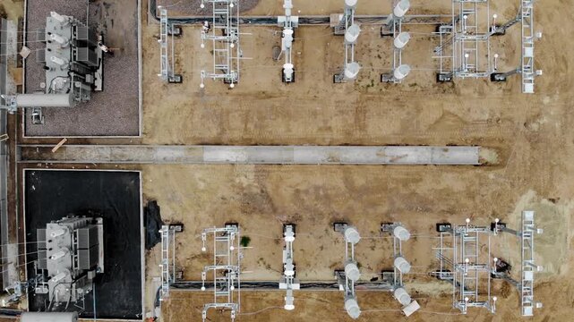 Aerial drone view of an electrical substation under construction in Sumy, Ukraine. High-voltage transformers, switchgear, transmission equipment, utility buildings, workers, and a yellow excavator