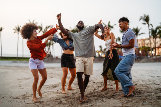 Energetic young people dancing with joy on the sandy beach at sunset, celebrating summer and freedom