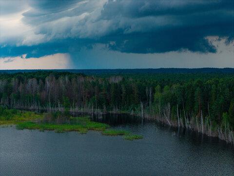 Aerial view of Kalnciema dolomite quarry surrounded by dense forest and dark storm clouds with heavy rain falling in the distance in Valgunde Parish, Jelgava Municipality, Latvia.