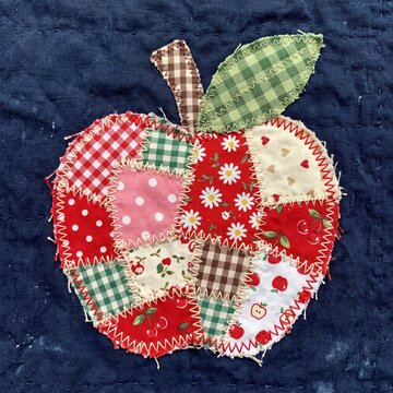 Fabric patchwork apple applique with zigzag stitches and varied patterns on a navy blue quilted background, handmade sewing craft.