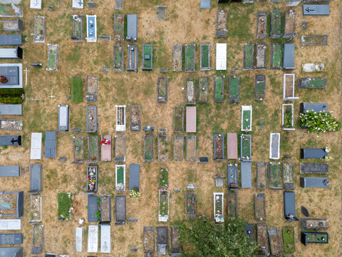 Aerial view of Gunnersbury Cemetery featuring rows of gravestones and monuments arranged in a geometric pattern across dry grass in London, England, United Kingdom.