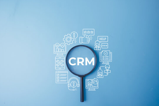 CRM Customer Relationship Management concept. Magnifying glass focusing on CRM text surrounded by digital customer service, helpdesk support, and feedback icons on a blue background.