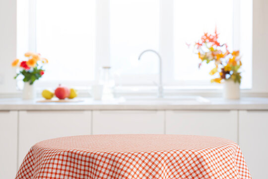 Red checkered tablecloth on table as empty design space of blurred kitchen interior
