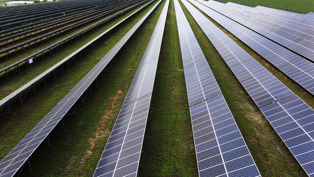 Solar farm generating clean electricity with long rows of photovoltaic panels on green grass for sustainable energy