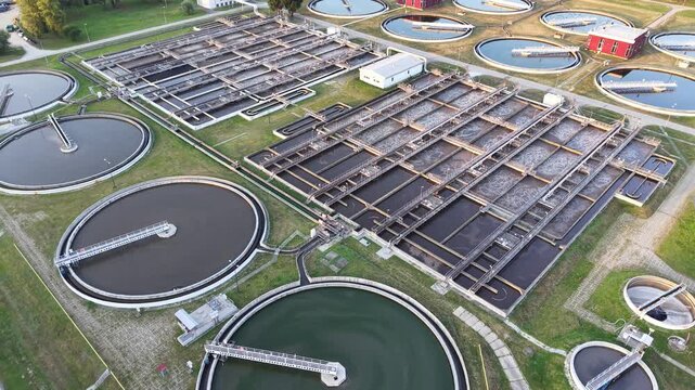 Aerial view of a water purification facility showcasing multiple circular and rectangular treatment tanks, surrounded by green grass and buildings, illustrating the process of water treatment and puri