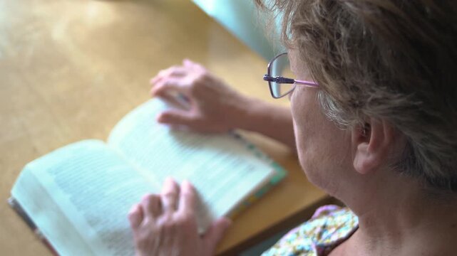 Back view from behind of a senior woman reading a book closeup