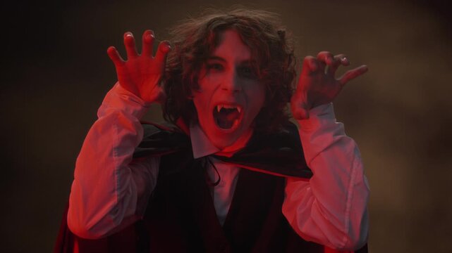 Portrait of Caucasian teenager wearing vampire costume with fangs, gesturing spookily at camera. Clip is perfect for Halloween retail advertisements and spooky holiday marketing