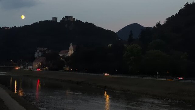 Full moon over the scenic Celje river embankment promenade with evening traffic and calm atmosphere