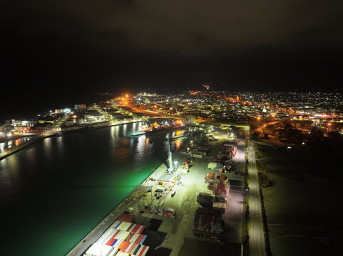 Aerial view of Timaru Port at night, featuring illuminated shipping containers, industrial cranes, and the glowing city lights along the coastline in Timaru, Canterbury Region, New Zealand.