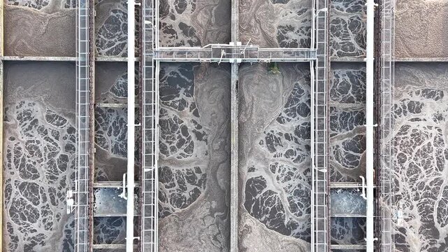 Aerial view of a water purification system showing sedimentation tanks with swirling water and foam, highlighting the continuous flow of water treatment processes in an industrial setting