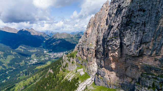 Aerial view of the dramatic limestone peaks of the Dolomites towering over the lush green valley and the village of San Martino di Castrozza, Trentino-Alto Adige, Italy.