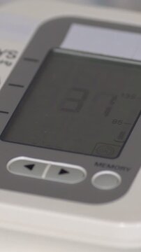Close up view of an automatic digital tonometer measuring blood pressure, with systolic and diastolic numbers changing on the lcd screen during a routine health examination