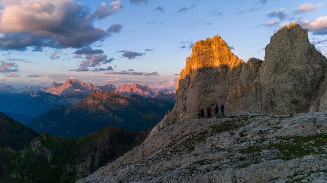 Aerial view of the Dolomites at golden hour with a group of people standing on a rocky peak overlooking the mountain range, San Martino di Castrozza, Trentino-Alto Adige, Italy.
