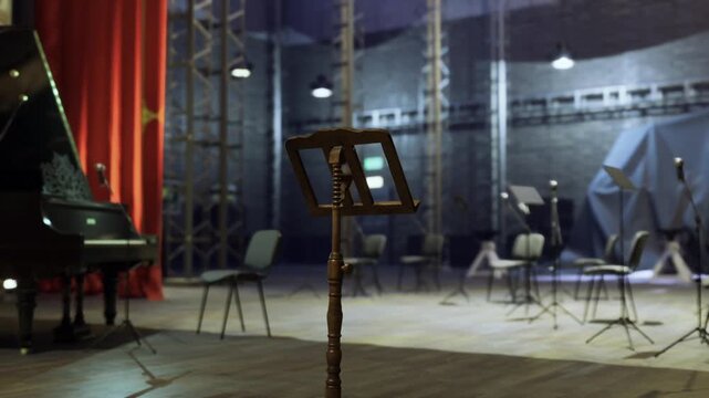 Empty rehearsal stage with piano, red curtain and vintage music stand center, scattered chairs, industrial rigging in background, soft spotlights creating moody