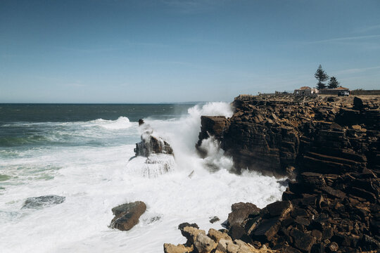 Powerful ocean waves crashing violently against steep rocky cliffs in Peniche, Portugal, creating massive sea spra