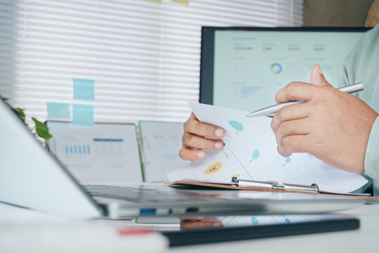 Business professional reviewing analytics report with financial charts and KPI dashboard on computer monitor, strategic planning, performance analysis, data-driven decision making in modern office