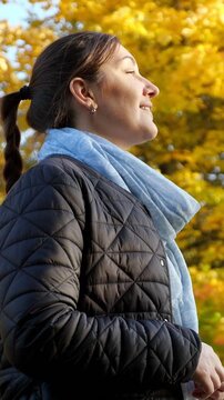 Peaceful young woman smiling with her eyes closed, enjoying the autumn sun and fresh air in a park. Relaxed and happy lady finding a moment of calm, freedom, and mindfulness in nature