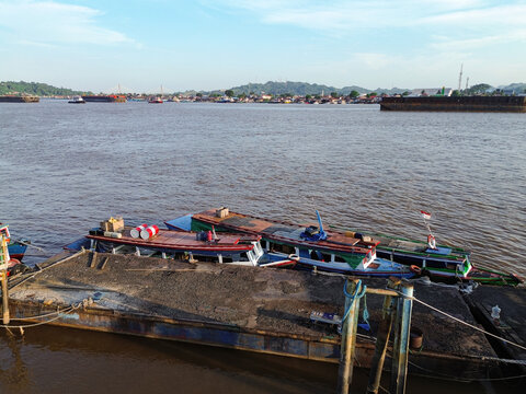 Aerial view of Pelabuhan Samarinda with traditional wooden boats moored at a concrete pier on the Mahakam River, with barges in the background in Samarinda Kota, East Kalimantan, Indonesia.