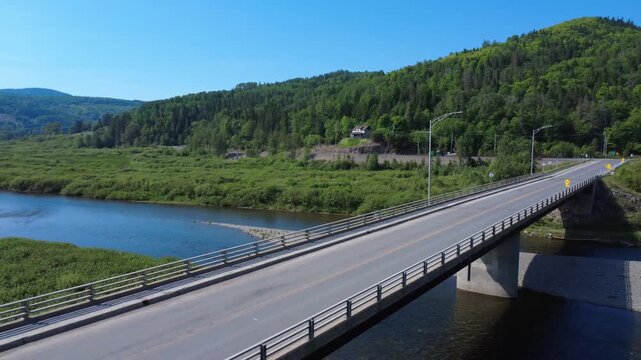 A red vehicle travels across a bridge spanning the picturesque Matapedia River.