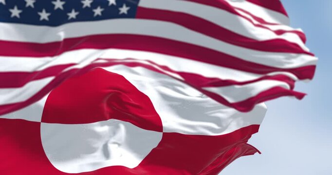 Flags of Greenland and the US waving in the wind on a clear day