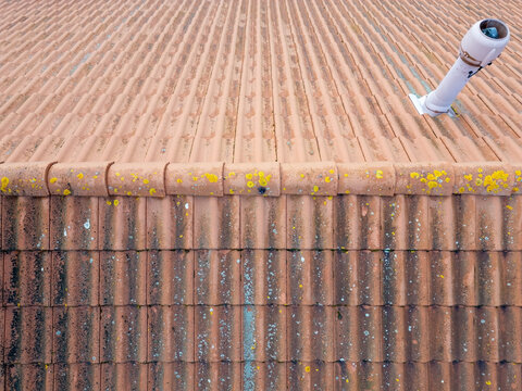 Aerial view of terracotta roof tiles covered with yellow lichen and a white ventilation pipe in Kempele, North Ostrobothnia, Finland.