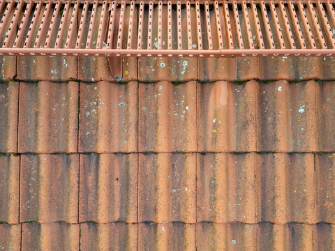 Aerial view of weathered orange clay roof tiles covered in patches of lichen and moss with a metal snow guard in Kempele, North Ostrobothnia, Finland.