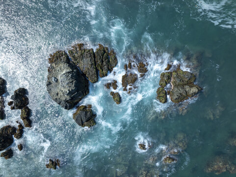 Aerial view of rugged dark rocks surrounded by turquoise ocean waves crashing against the coast in Zihuatanejo, Guerrero, Mexico.