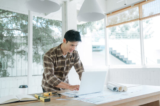 Architect working at a laptop with architectural blueprints in a modern studio, representing building design, construction planning, engineering, and professional project development.