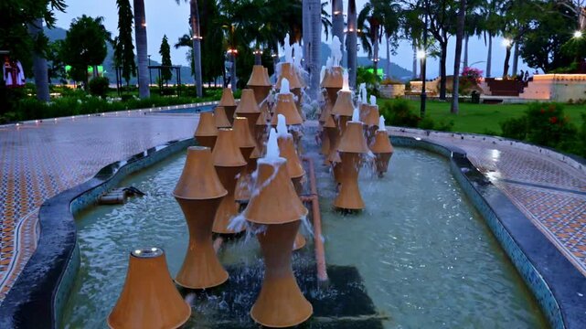 Modern water jets dance under colorful accent lighting. Tall palms surround the stone paths. Tranquil atmosphere rests on Fateh Sagar Lake in Udaipur, Rajasthan.