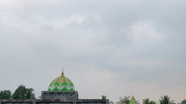 Dark clouds moving quickly above a mosque with a green dome in a dramatic time lapse, symbolizing changing weather and Islamic architecture.