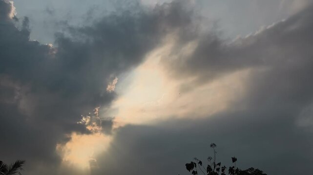 Sunlight filtering through dramatic storm clouds with dark cloud formations drifting across the sky, creating a cinematic weather background before rainfall.