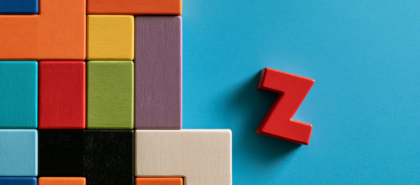 Elegent photo of Colorful wooden block shapes arranged in a puzzle pattern with a red letter Z on a blue background. This symbolizes creative problem solving and learning concepts.