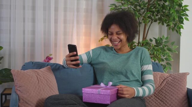 Happy african american woman receiving a birthday gift during a video call