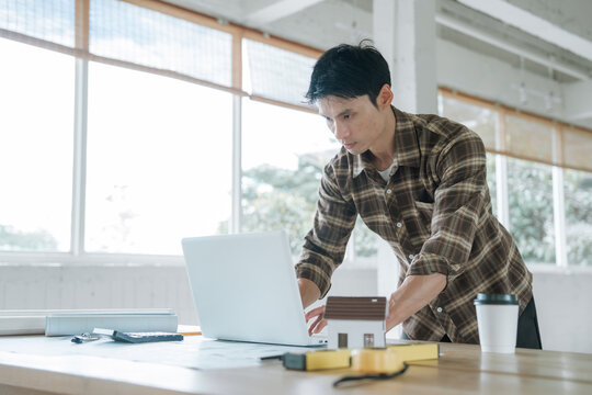 Architect working at a laptop with architectural blueprints in a modern studio, representing building design, construction planning, engineering, and professional project development.