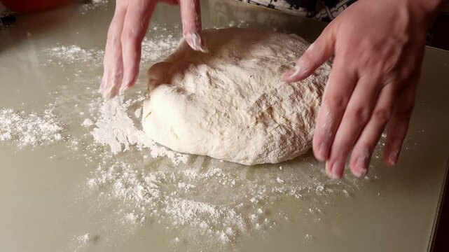 Close-up of hands skillfully kneading a ball of raw dough on a floured countertop, showing the texture and process of bread making