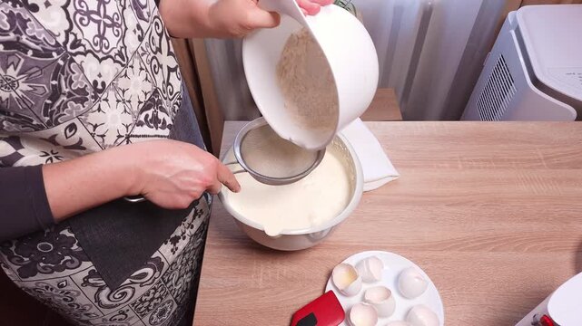 A woman carefully mixing ingredients in a bowl with a spatula, preparing dough for a culinary product.