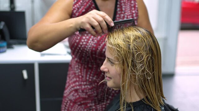 Hairdresser combing woman's wet blonde hair