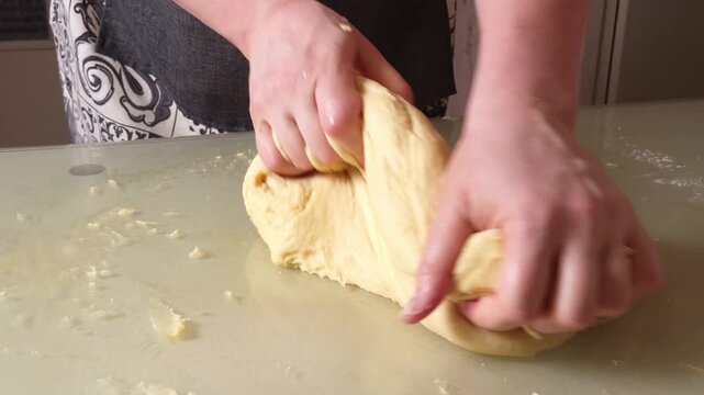 Close-up of hands actively working and kneading a ball of dough on a smooth, light-colored surface, preparing for baking
