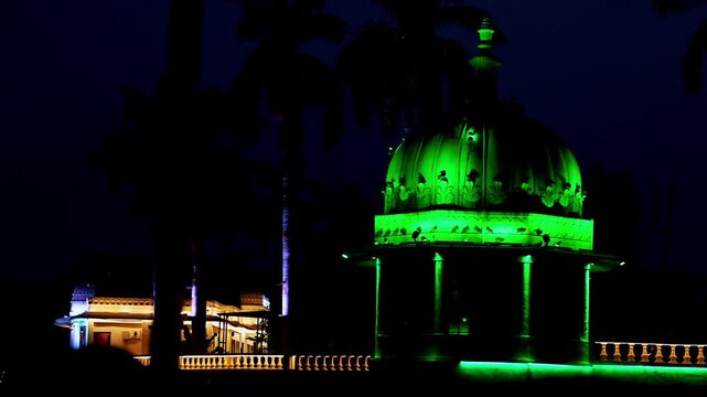 Beautiful lighting setups illuminate the island garden against dark skies. Soft glows spread over calm waters. Serenity envelops Fateh Sagar Lake in Udaipur, Rajasthan.