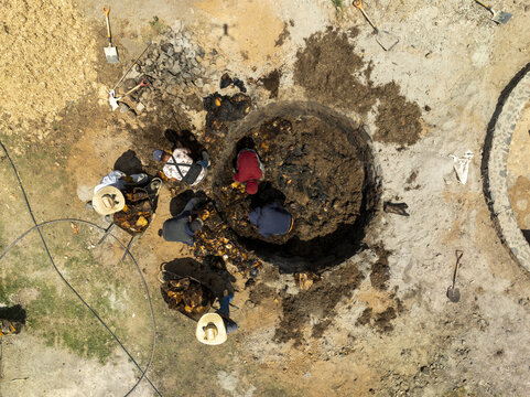 Aerial view of workers preparing an underground mezcal oven with agave hearts and shovels in the traditional production process in Oaxaca, Oaxaca, Mexico.