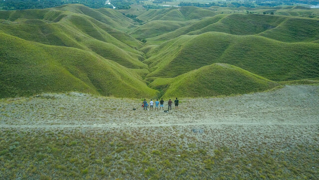 Aerial view of a group of people standing on a ridge overlooking rolling green hills in Indonesia.