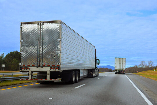 Trucks travel on highway near mountains on cloudy day