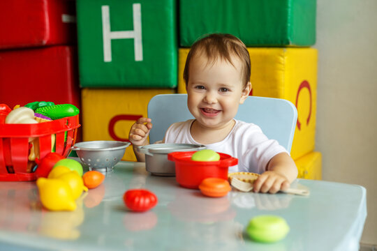 Happy toddler enjoying pretend cooking game with toy food at daycare