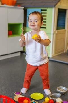 Smiling toddler holding toy lemon during pretend kitchen play at daycare