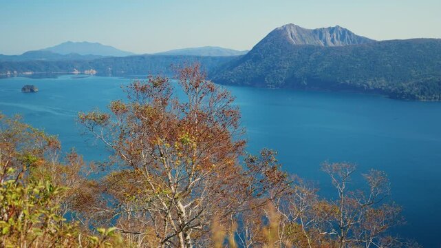 Stunning aerial view of the volcanic caldera Lake Mashu in Akan Mashu National Park, Hokkaido, Japan, showing the deep blue water and surrounding mountains during a sunny autumn day
