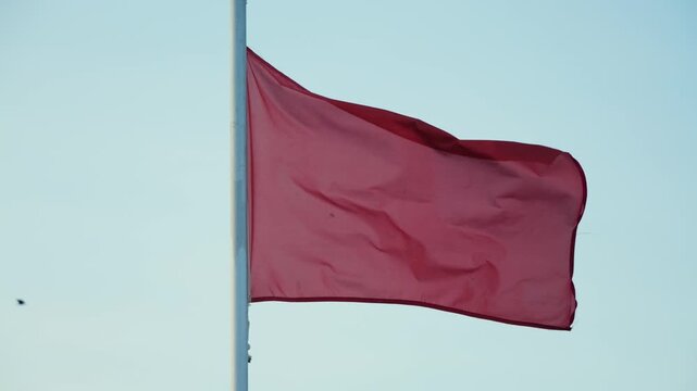 Red warning flag flying on a beach against a clear blue sky, indicating dangerous swimming conditions and restricted access to the water. Coastal safety and summer beach concept. High quality 4k