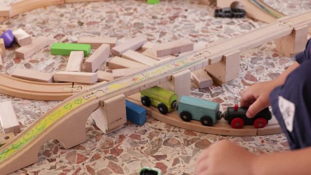 Close up of a child's hands playing with a wooden toy train on a track at home, then father's hand appears to help. Fine motor skills, early education, and father-son play concept