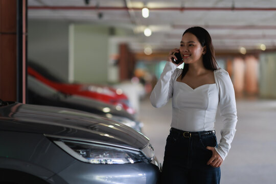 Young Asian woman confidently walking and talking on her smartphone in an urban underground parking lot, communicating with a client or friend while smiling