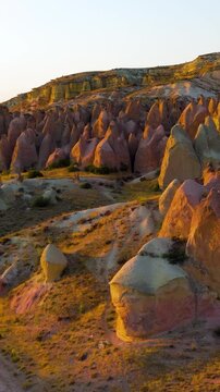 Vertical video. Goreme, Nevsehir, Turkey. Devrent Valley fairy chimneys and eroded volcanic tuff formations, aerial view at golden hour with warm light sculpting the mineral-rich landscape. Aerial Vi