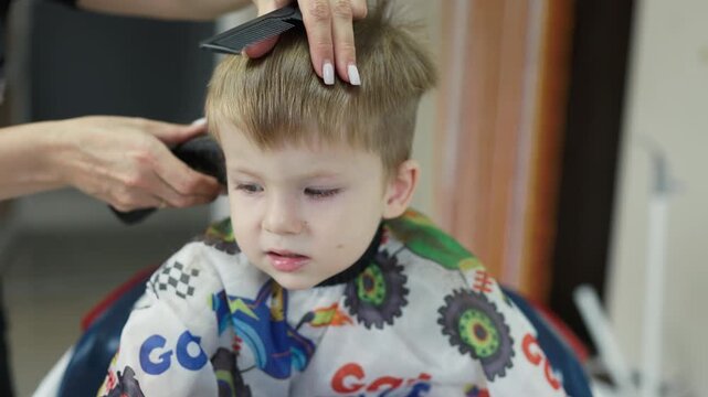 Little boy getting a haircut with hair clipper at kids barbershop
